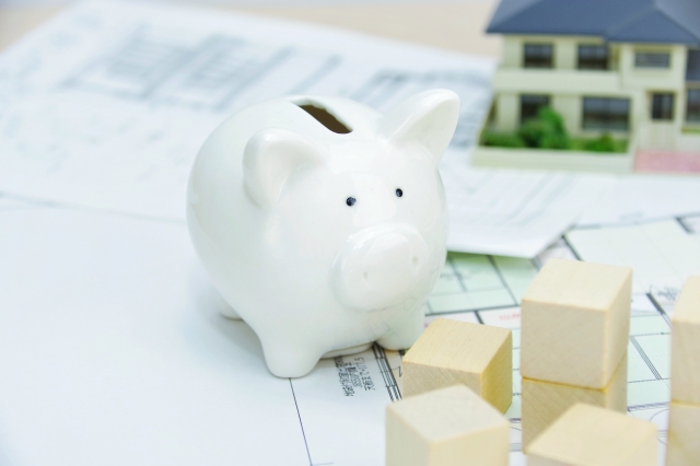 住宅の図面に置かれた貯金箱と住宅模型