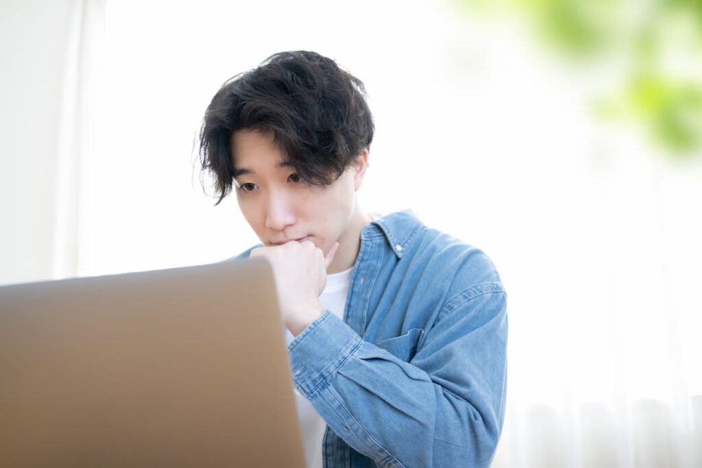 ノートパソコンを見ながら考える男性
