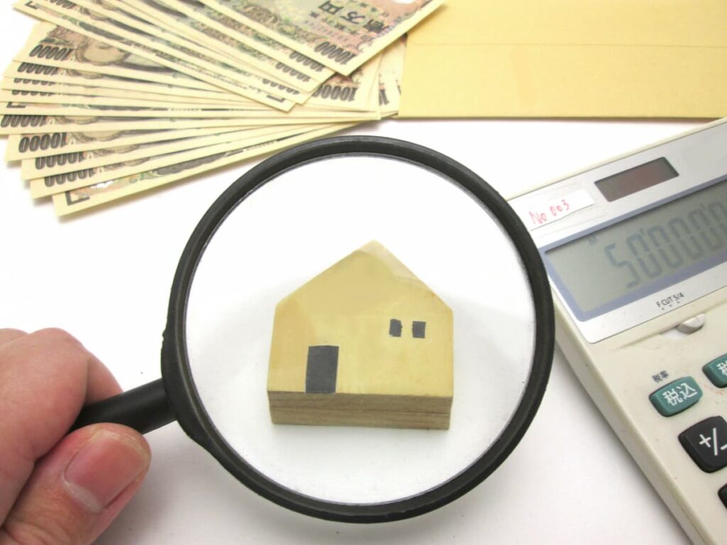 虫眼鏡で確認する住宅模型と電卓、紙幣