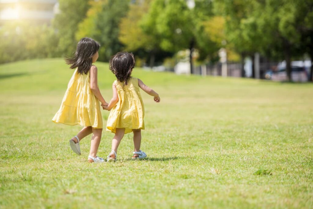 芝生の公園を手をつないで歩く二人の女の子