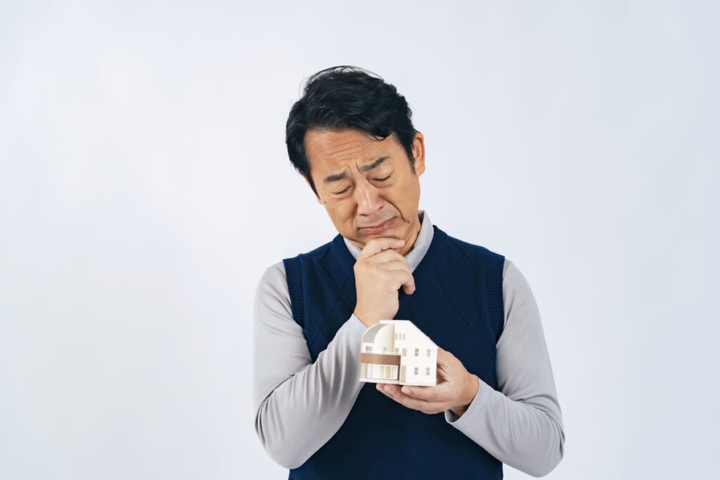 住宅模型を手に持って悩む男性
